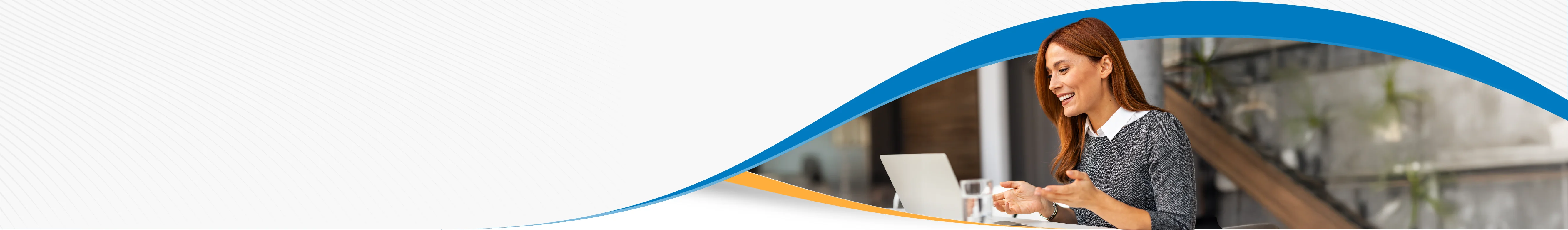 Woman with a white collar shirt and grey sweater is smiling and presenting information while sitting at a desk with a laptop