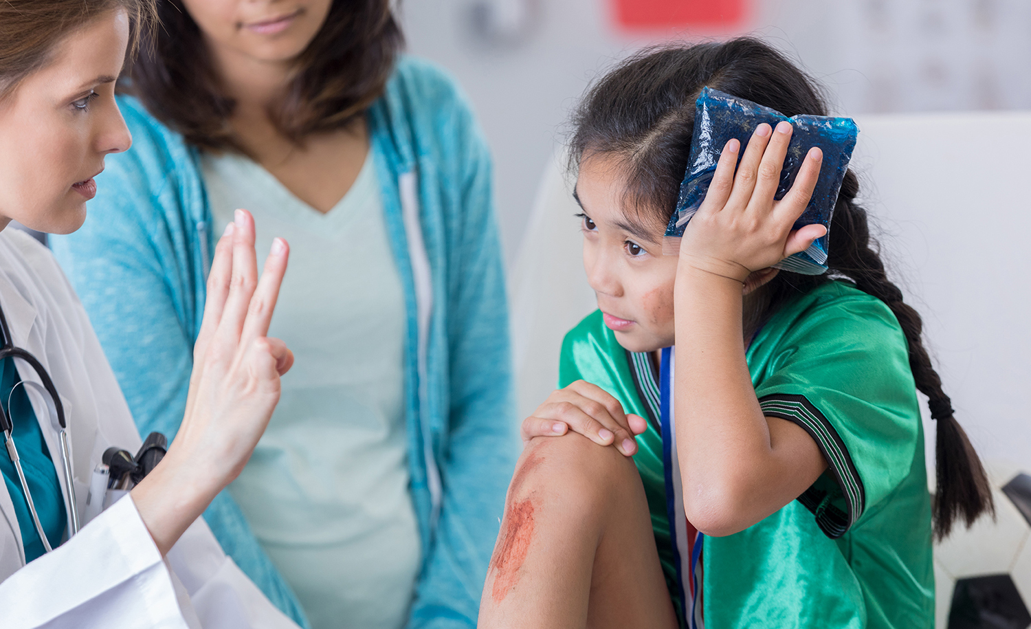 A young girl holding an ice pack to her head while being treated by a doctor.