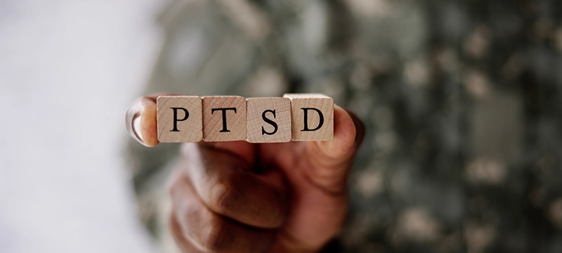 A person holds up wooden blocks of the letters PTSD, representing PTSD awareness