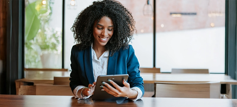 A professional woman in an office setting smiles while looking down at a tablet, representing the value of the digital record form and how it makes test administration easier